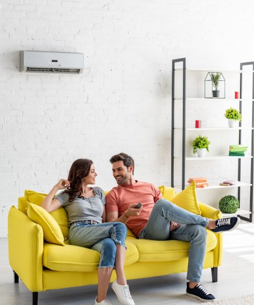 young man and woman talking while sitting on yellow sofa under air conditioner at home